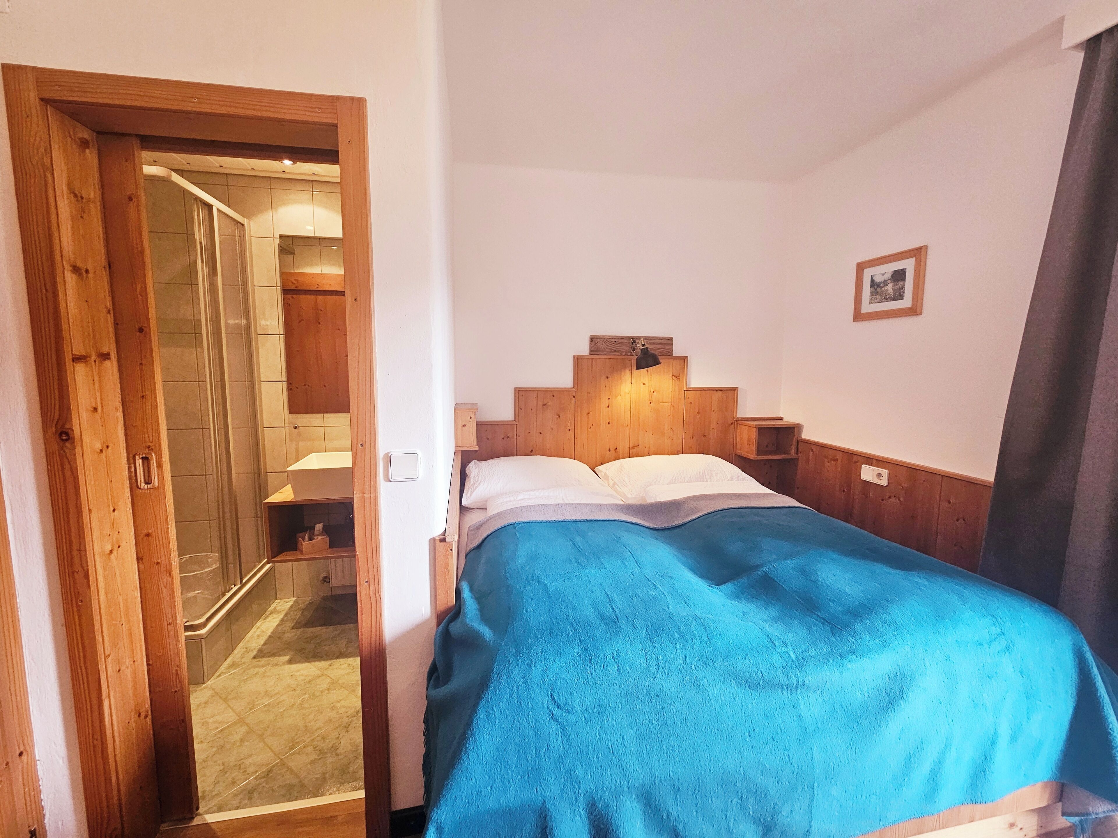 A bedroom with a wooden headboard, a bed with a blue blanket, a nightstand, and a small shelf.