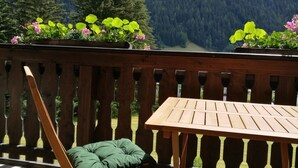 A wooden deck with a table and a folding chair, overlooking a forested mountain.