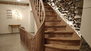 A wooden staircase with a stone wall backdrop, a small table, and wall-mounted lights.