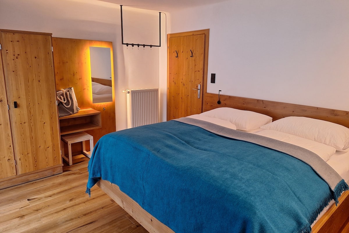 A bedroom with a wooden bed, a blue blanket, a wooden wardrobe, a mirror, and a radiator.