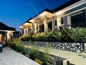A residential building with a covered porch, a stone wall with a geometric pattern, and a paved walkway.