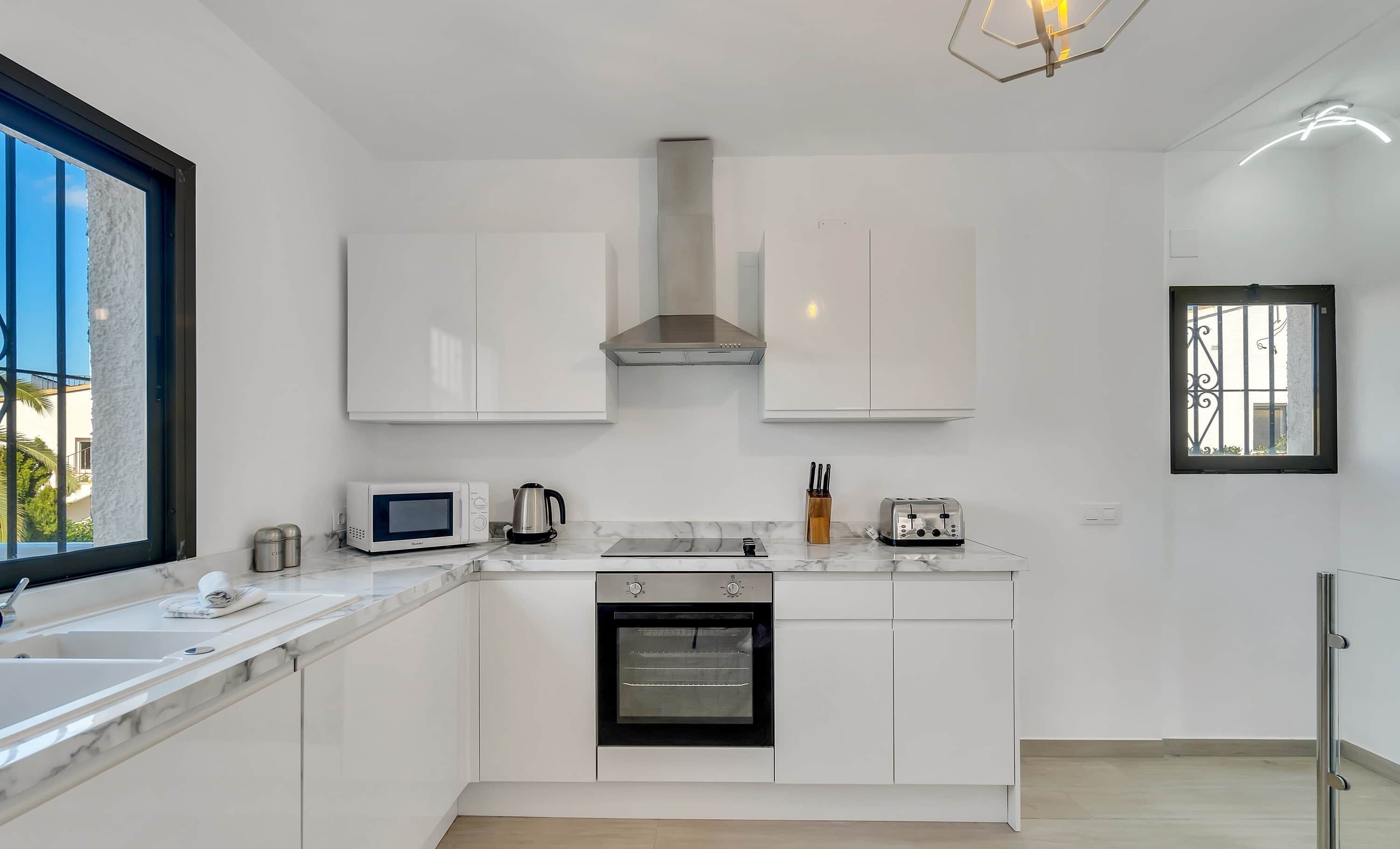 A modern kitchen with white cabinets, a microwave, a kettle, a toaster, and an oven.