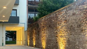 A paved walkway leading to a building entrance with a stone wall and modern lighting. - GuestHouse Große Linde (Karlsruhe)