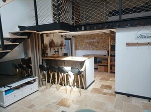 A compact kitchen with a bar area, a dining set, and a staircase leading to a loft. - Ideal for curists, old barn of 50m2 restored with all comforts. (Casteljaloux)