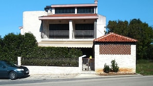 En toetages bygning med balkon, et mindre tilbygget hus med tagsten, og en bil foran.