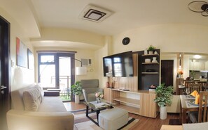 A modern living room with a sofa, a coffee table, a TV, and a dining area with a table and chairs. - 1BR KLASSI Comfort Stay (Pasay)
