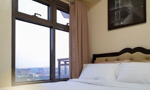Ein Hotelzimmer mit großem Fenster, einem Bett mit weißer Bettwäsche und einem gerahmten Bild an der Wand.