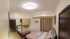 A hotel room with a bed, a mirror, a wardrobe, a bedside table, a ceiling light, and an air conditioning unit.