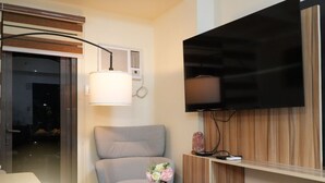 A modern living room with a flat-screen TV, a grey sofa, a table with a vase of flowers, and a wooden cabinet.