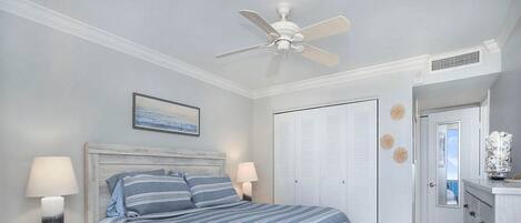 A bedroom with a bed, nightstands, a ceiling fan, a wardrobe, and a dresser.