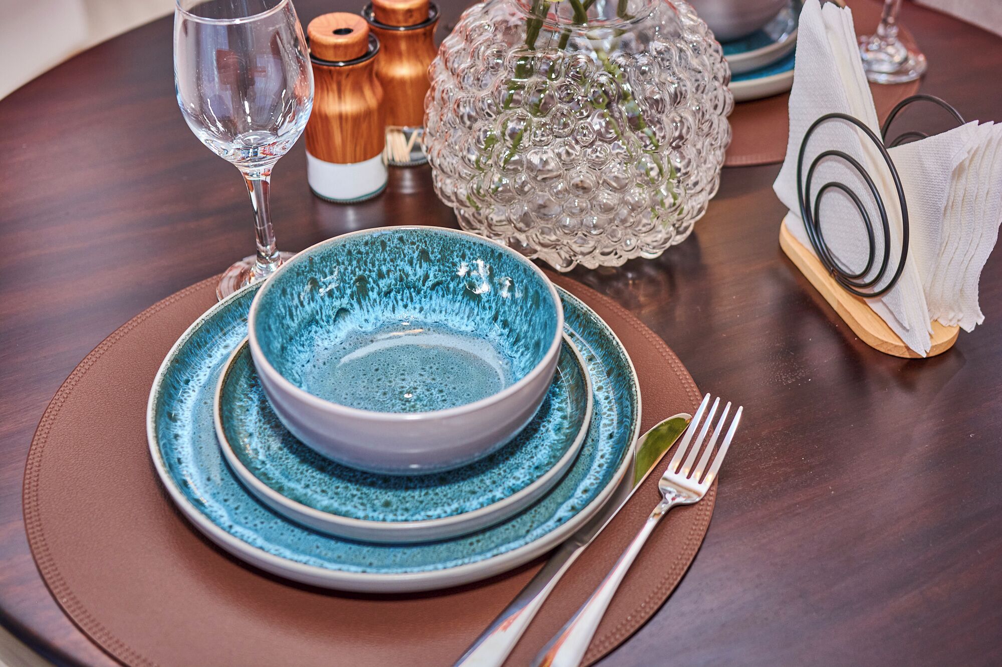 A dining table set with a blue bowl, a wine glass, and a fork.