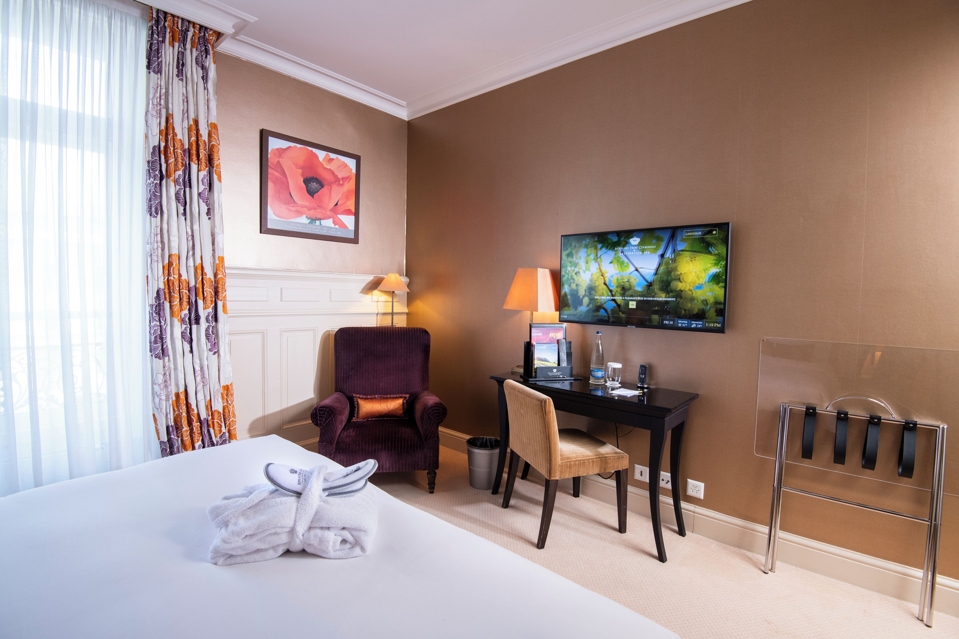 Een hotelkamer met een bed, een bureau met een computer, een stoel, een televisie en een raam met gordijnen.