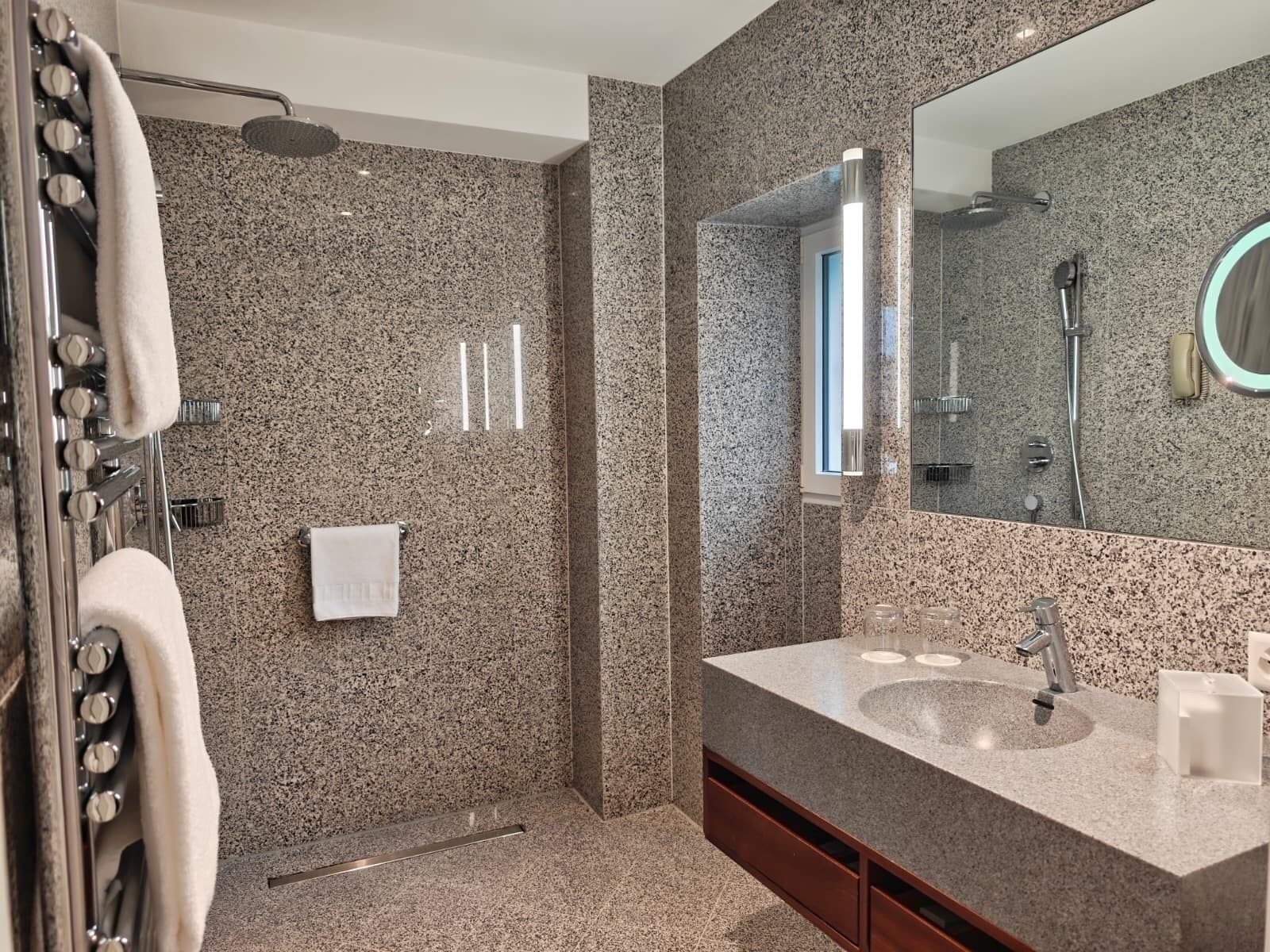 Un baño moderno con encimera de granito, un espejo grande, ducha y perchero.