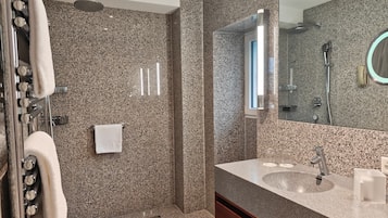 Un baño moderno con encimera de granito, un espejo grande, ducha y perchero.