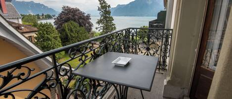 A balcony with a table and chair, overlooking a lake and mountains.