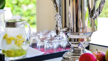 Un samovar plateado sobre una mesa cerca de una ventana con vistas a la vegetación.