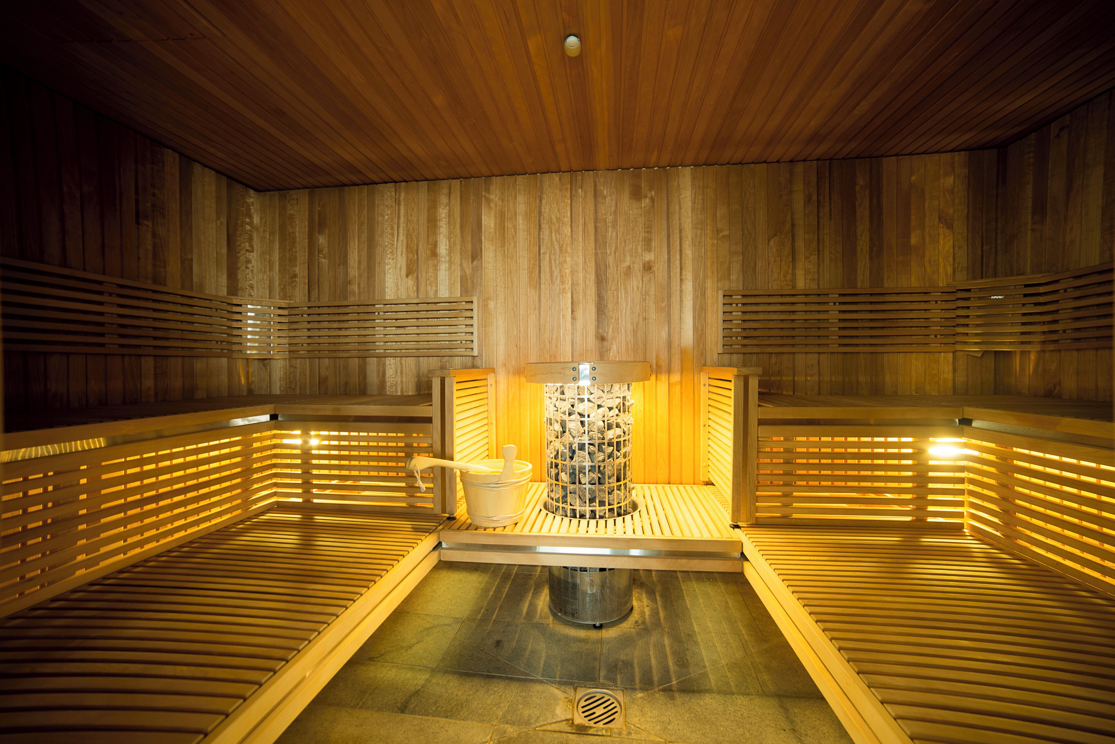 Eine Sauna mit Holzwänden und -bänken, einem zentralen Heizaggregat und einem kleinen Tisch mit einem Krug.