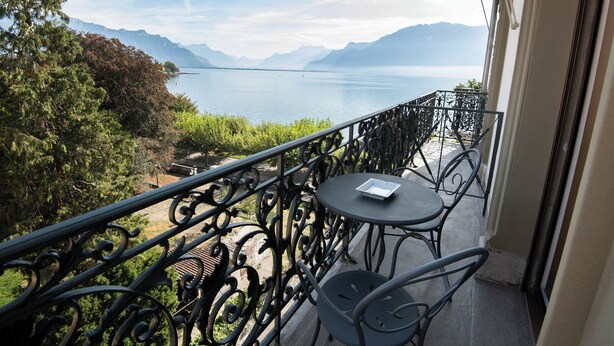 Un balcon avec vue sur un lac et des montagnes, une table et des chaises.