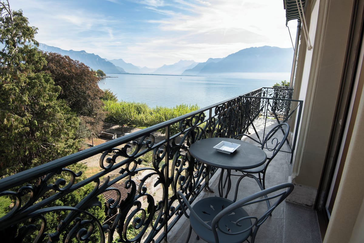 Un balcon avec vue sur un lac et des montagnes, une table et des chaises.
