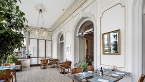 Une salle à manger avec des tables dressées, des chaises en bois, un lustre et un grand miroir au mur.