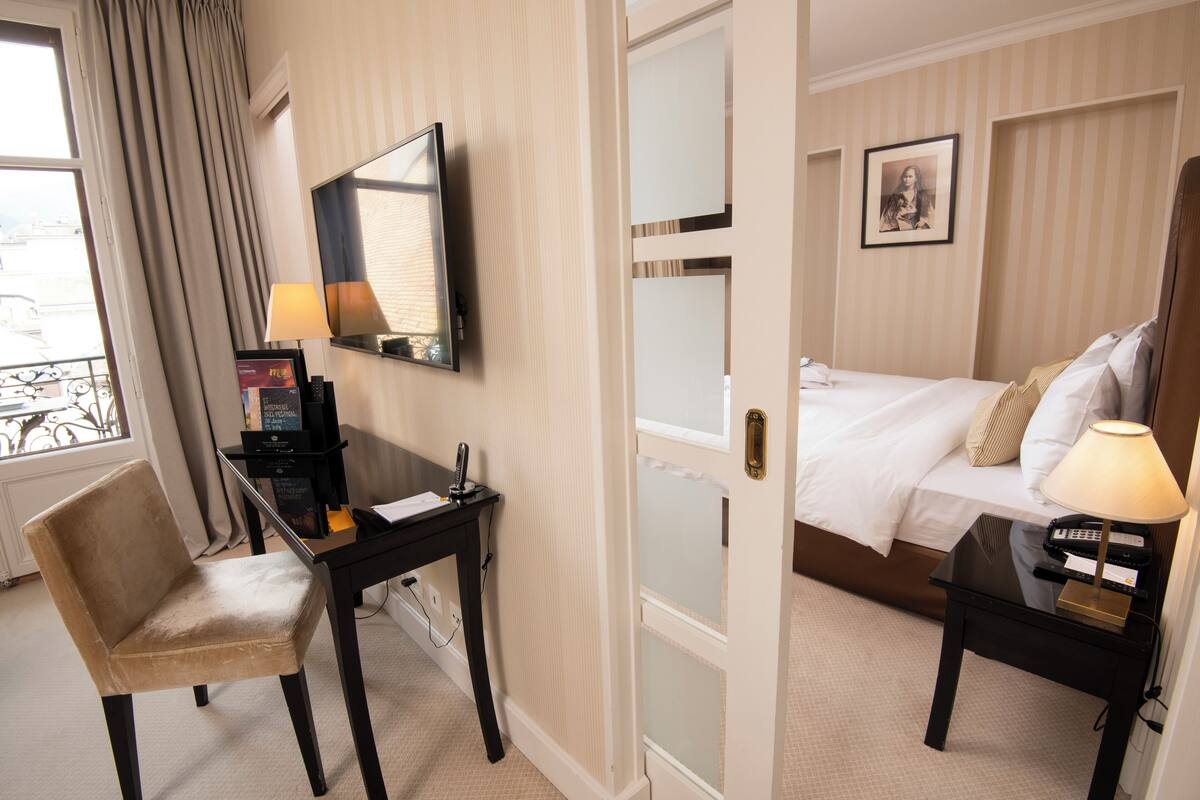 Une chambre d’hôtel avec un lit, un bureau avec une lampe, une chaise, une télévision et un tableau au mur.