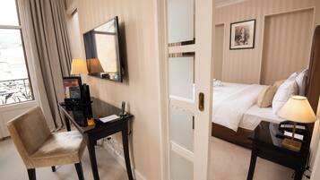 Una habitación de hotel con cama, escritorio con lámpara, silla, televisión y un cuadro en la pared.