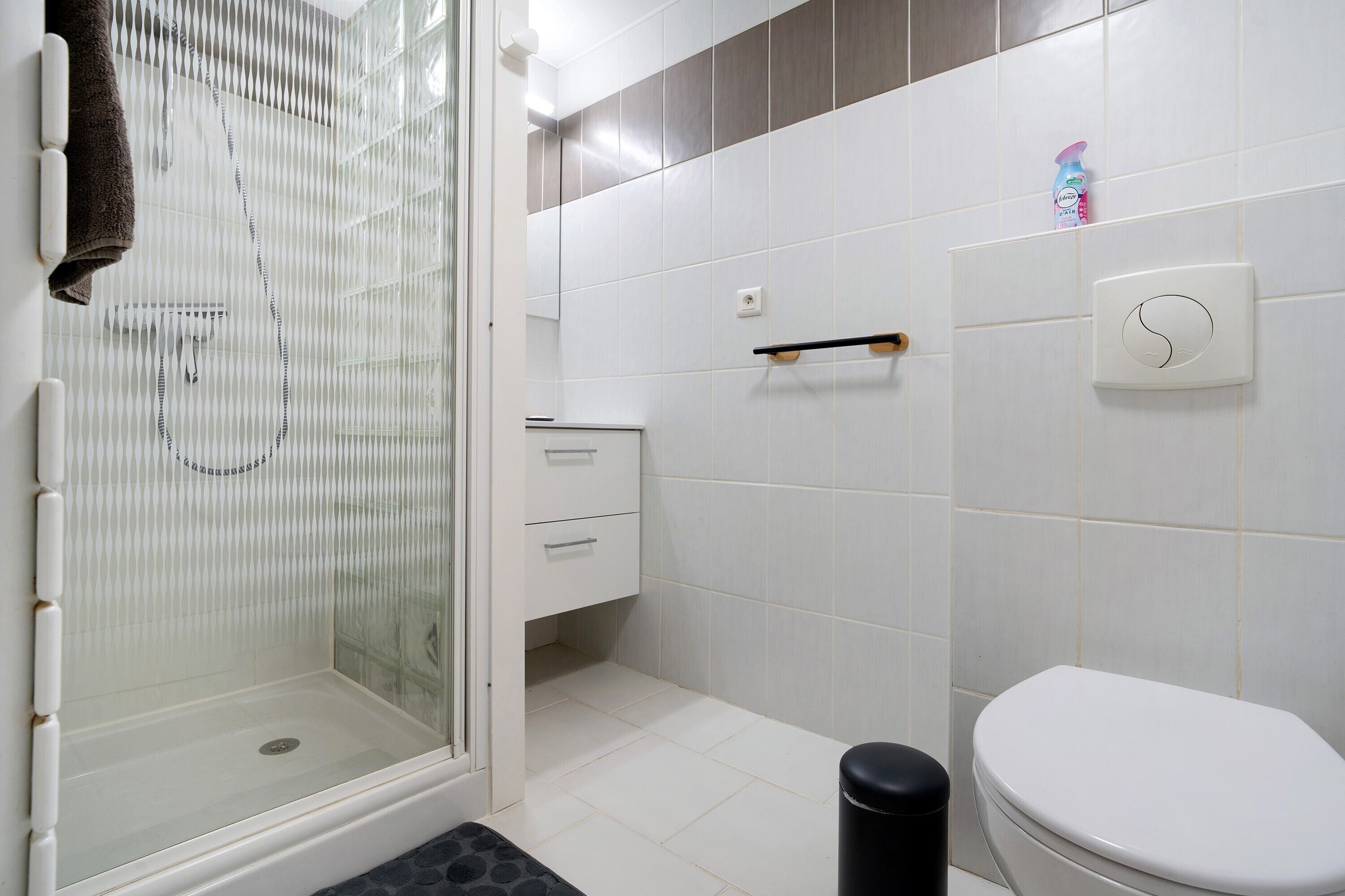 Une salle de bain avec une douche à parois de verre, des toilettes, un lavabo avec un porte-serviettes et un distributeur de savon fixé au mur.