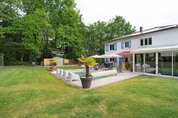 Une maison moderne dotée d’une piscine, d’un espace salon extérieur et d’une grande porte vitrée donnant sur un patio.
