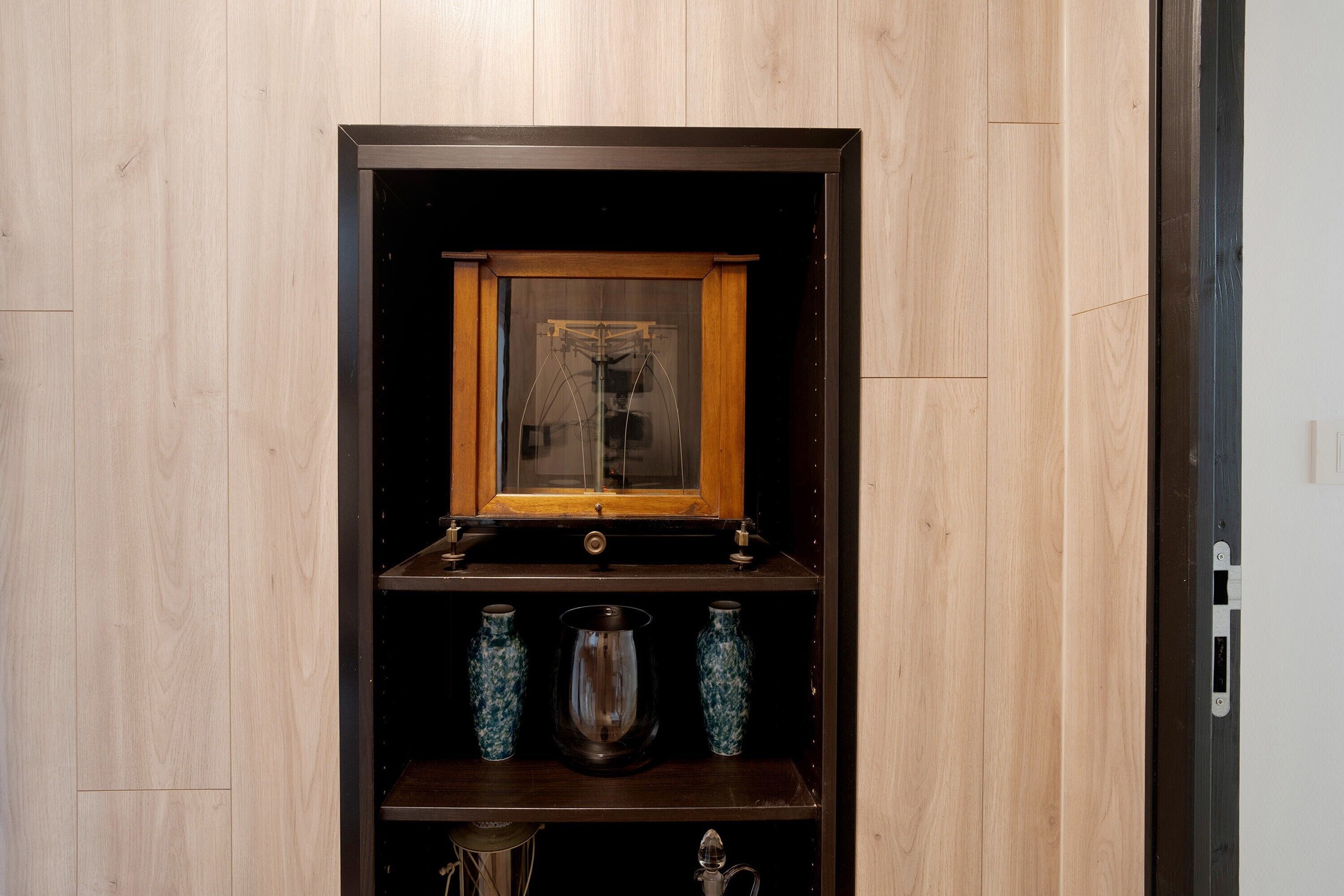 Een houten vitrinekast met glazen deuren, waarin zich drie blauwe decoratieve vazen en een metalen kan bevinden.