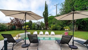 A poolside area with lounge chairs and umbrellas, a pool, and a well-maintained garden. - Villa Berthelots with Private Pool in Southern Charente (Montmoreau)