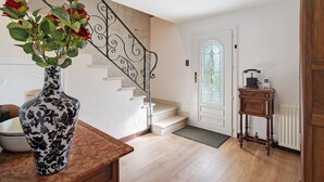 A staircase with a decorative railing, a white door with a glass window, and a wooden side table with a vase of flowers. - Villa Berthelots with Private Pool in Southern Charente (Montmoreau)