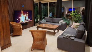 A modern living room with a flat-screen TV, a sofa, a coffee table, and wicker chairs. - Villa Berthelots with Private Pool in Southern Charente (Montmoreau)