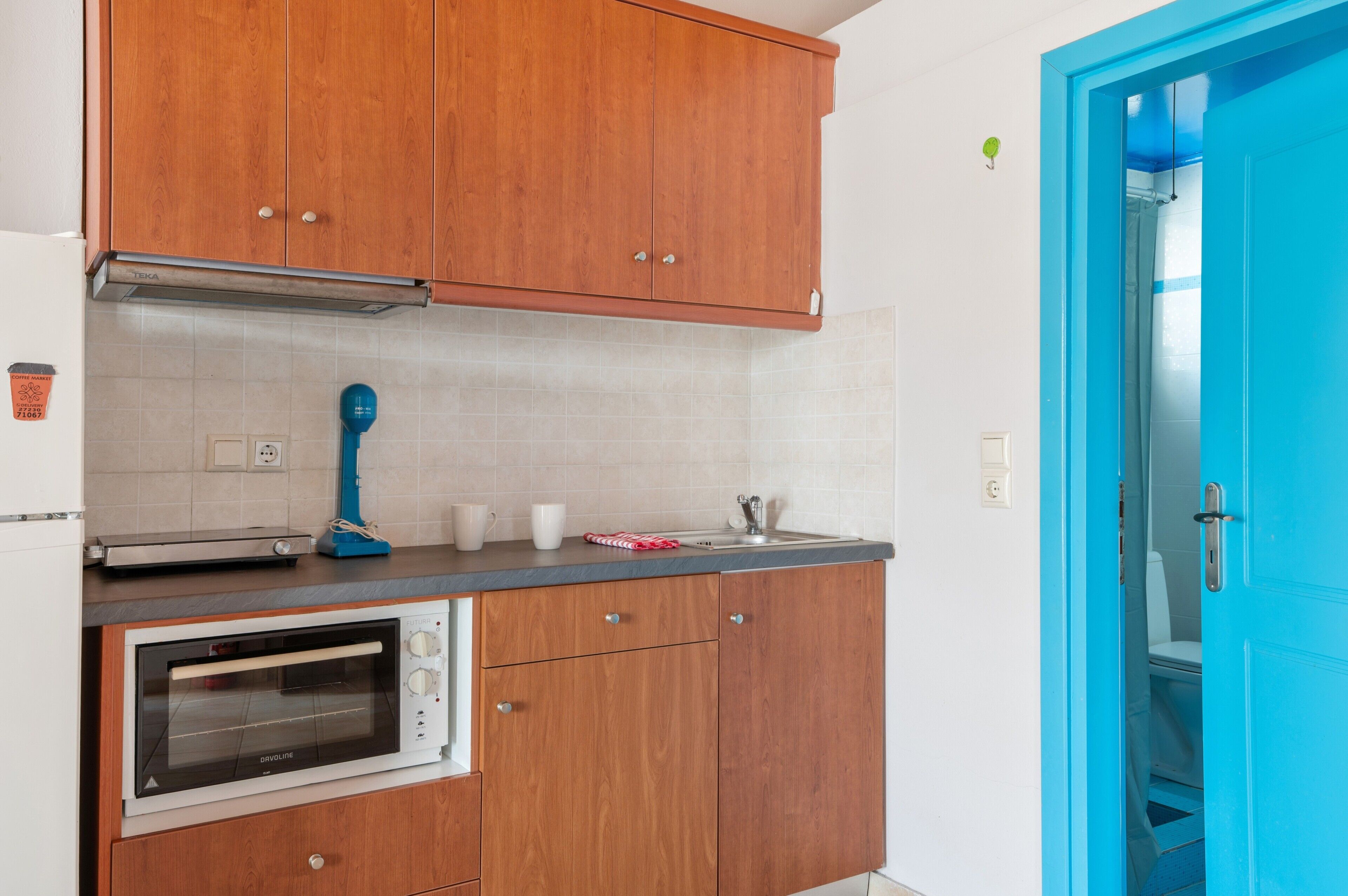 A kitchen with wooden cabinets, a built-in oven, a blue hairdryer, and a blue door.