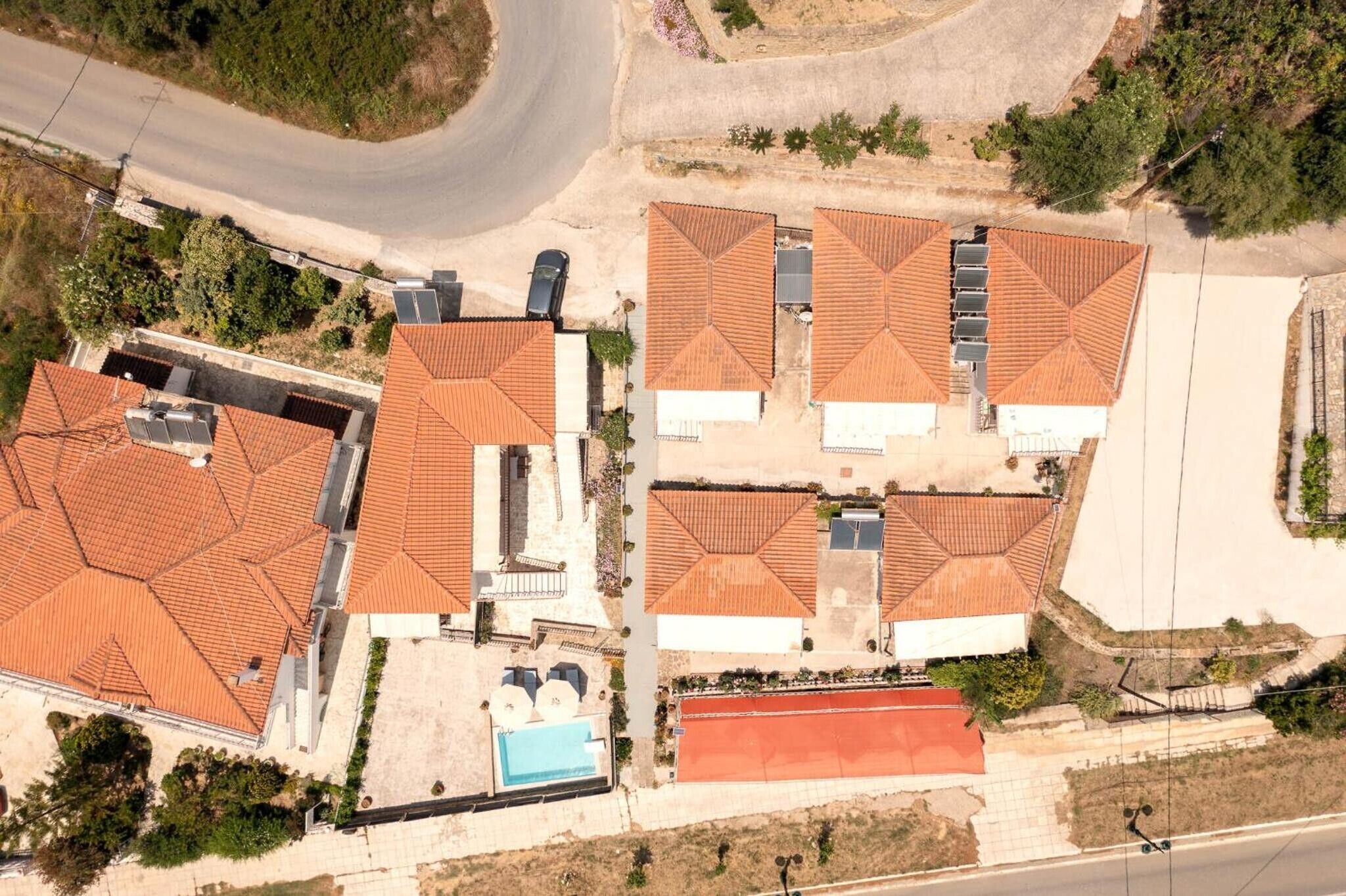Vista aérea de um bairro residencial com várias casas, telhados vermelhos, piscina e uma rua.