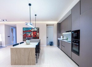 Et moderne køkken med en central ø, indbyggede apparater og et stort billede på væggen.