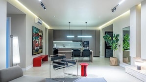 A modern living room with a sofa, a red stool, a black chair, and a dining area with a table and chairs. - Short Stays By CW (Lagos)