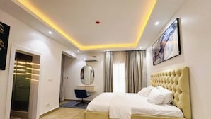 A modern bedroom with a large bed, a desk, a chair, a mirror, and a painting on the wall. - Short Stays By CW (Lagos)