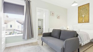 Ein Schlafzimmer mit grauem Sofa, einem Bett, einem Fenster mit Vorhängen und einem Gemälde an der Wand.