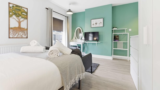 Ein modernes Schlafzimmer mit Bett, Schreibtisch, Fernseher und grüner Wand.