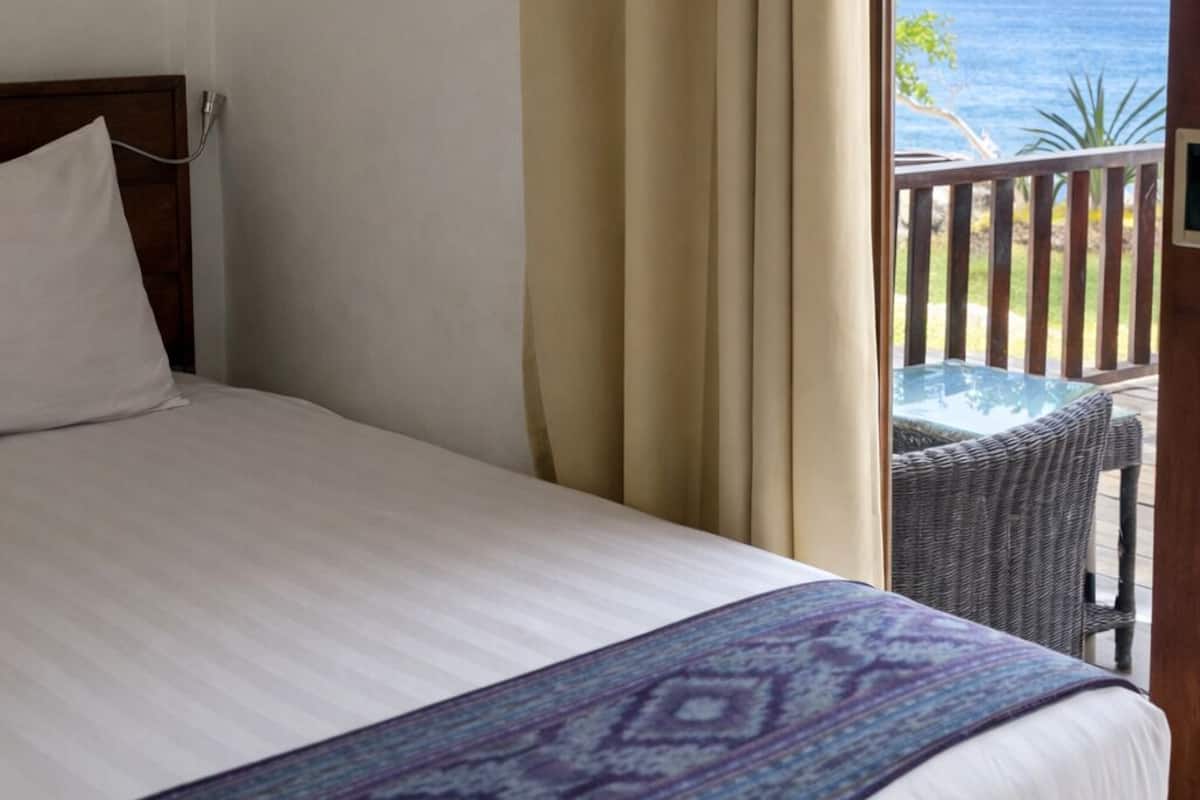A hotel room with a bed, a view of the ocean, and a balcony with a table and chairs.