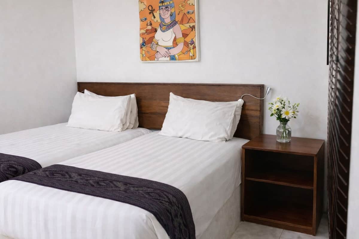 A double bed with white linens, a wooden headboard, and a nightstand with a vase of flowers.