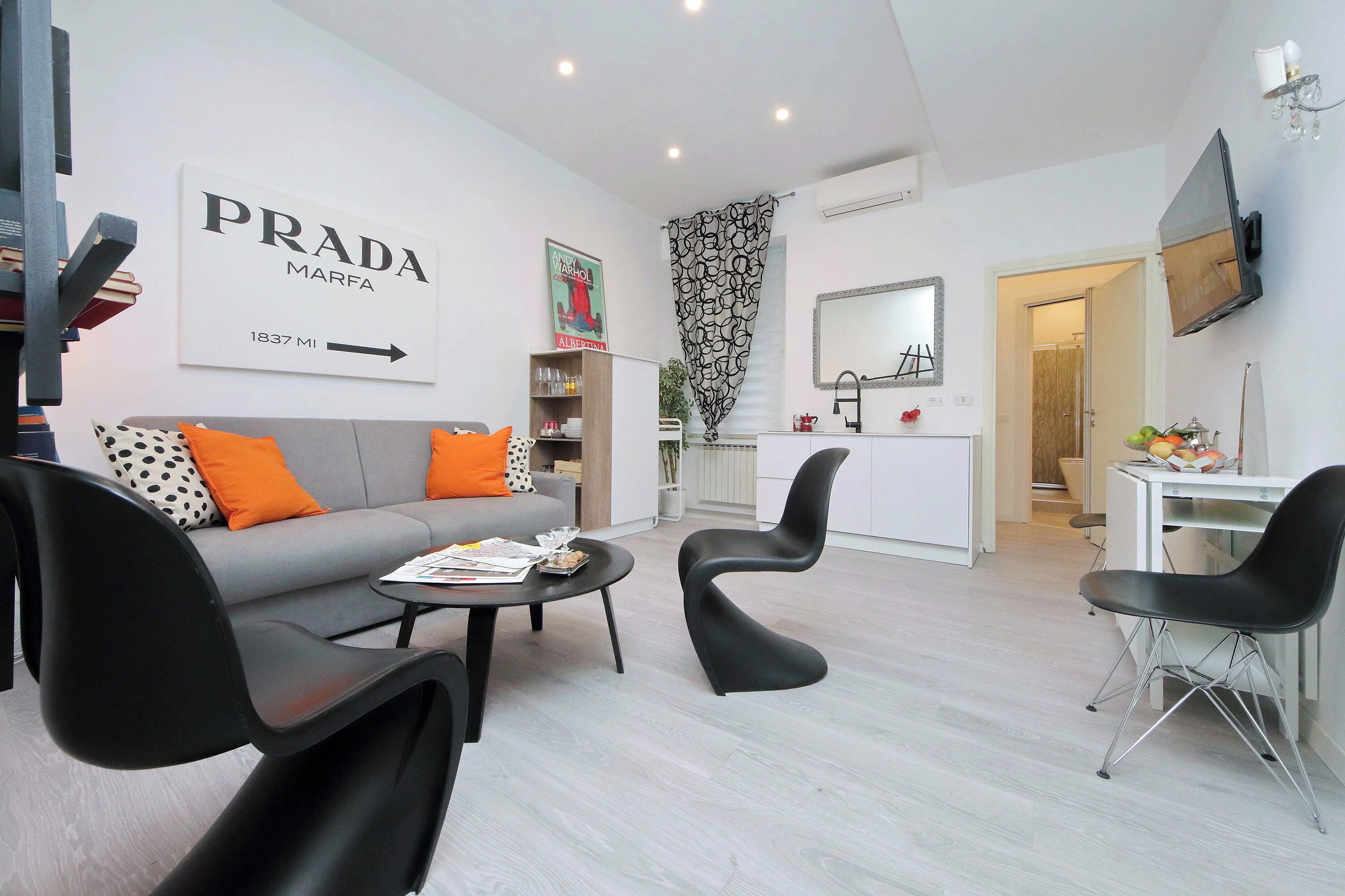 A modern living room with a sofa, two black chairs, a coffee table, and a TV mounted on the wall.