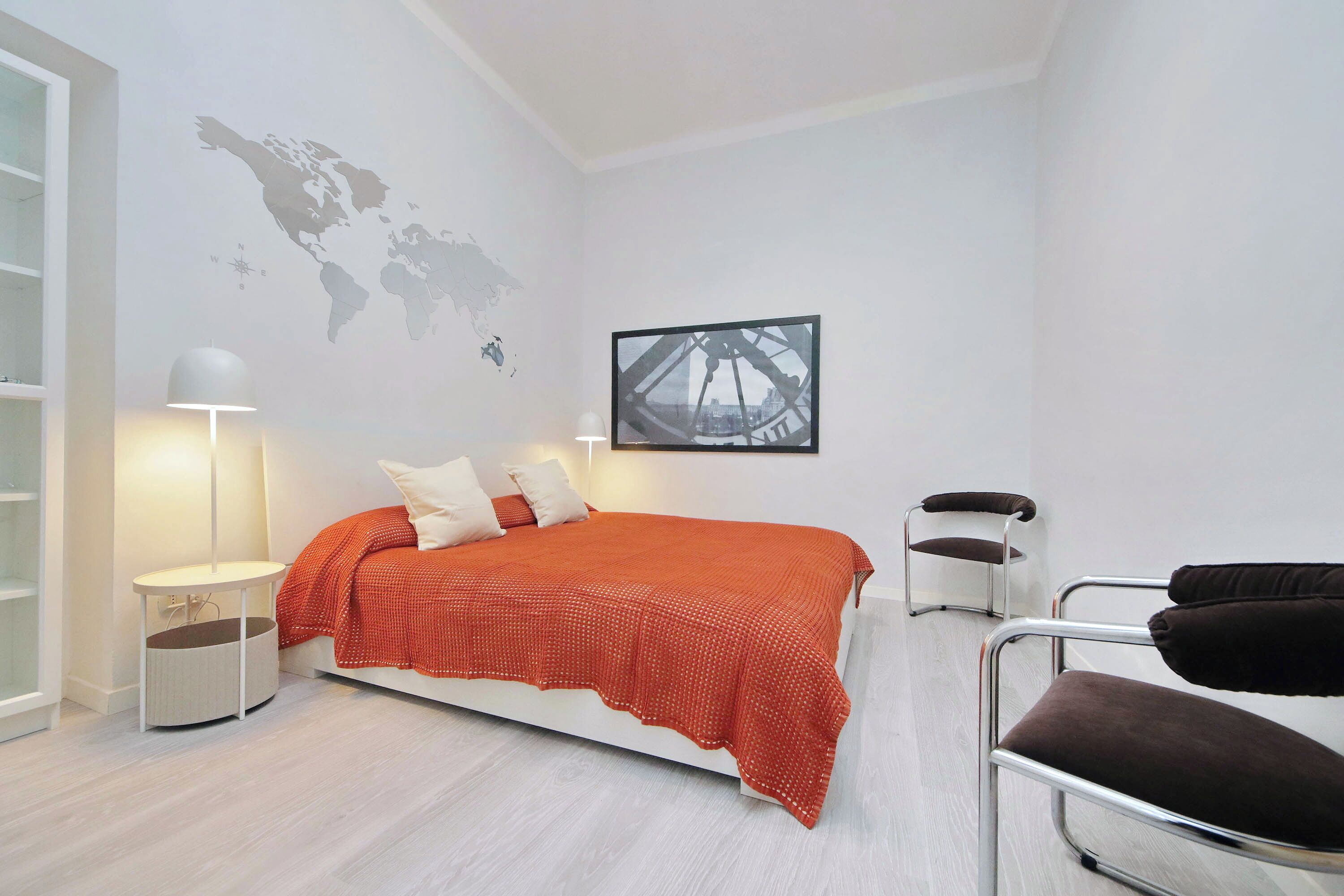A modern bedroom with a bed, a world map, a framed picture, a standing lamp, and a chair.