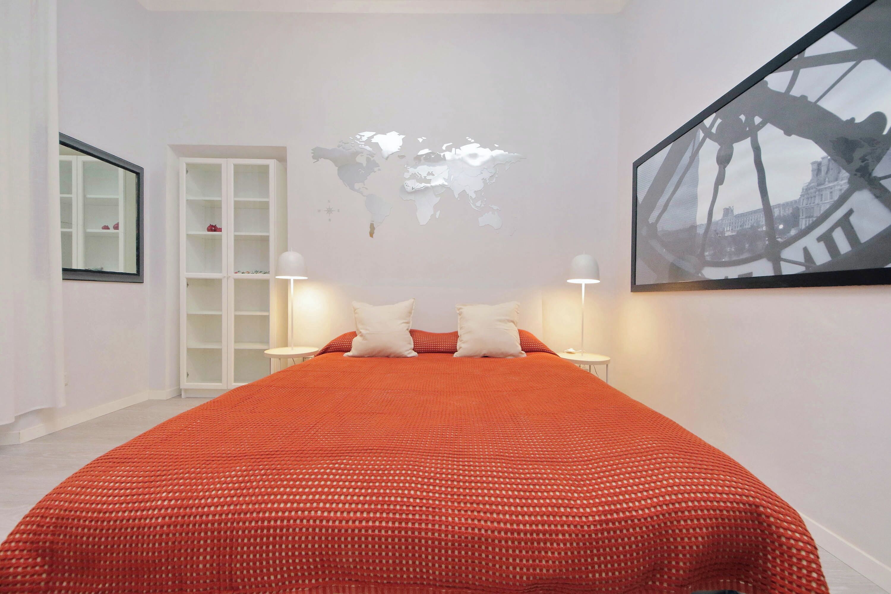 Une chambre d’hôtel bien rangée, avec un grand lit, une carte du monde accrochée au mur et un tableau encadré.