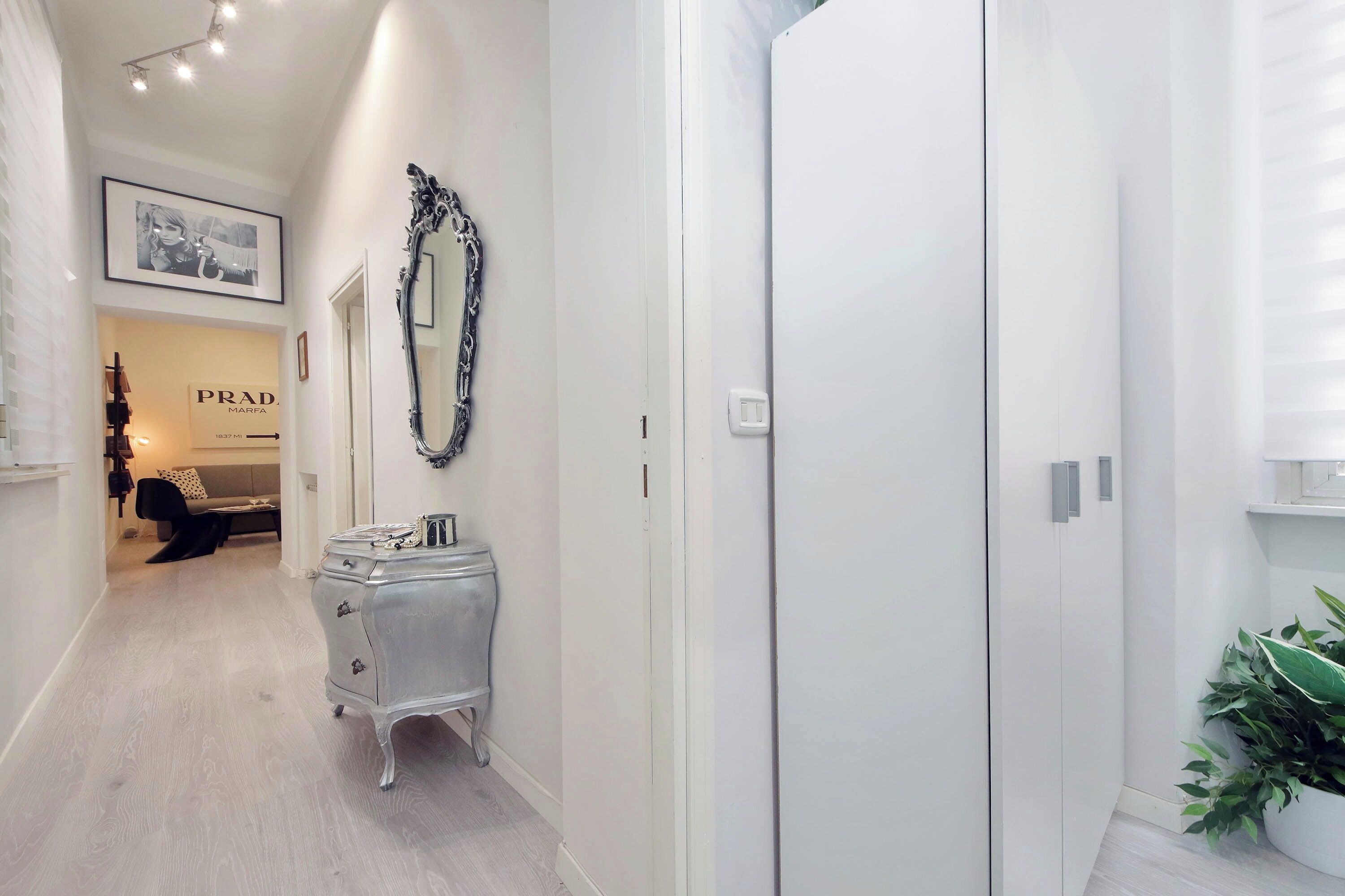 A hallway with a white wardrobe, a mirror, and a framed picture on the wall.