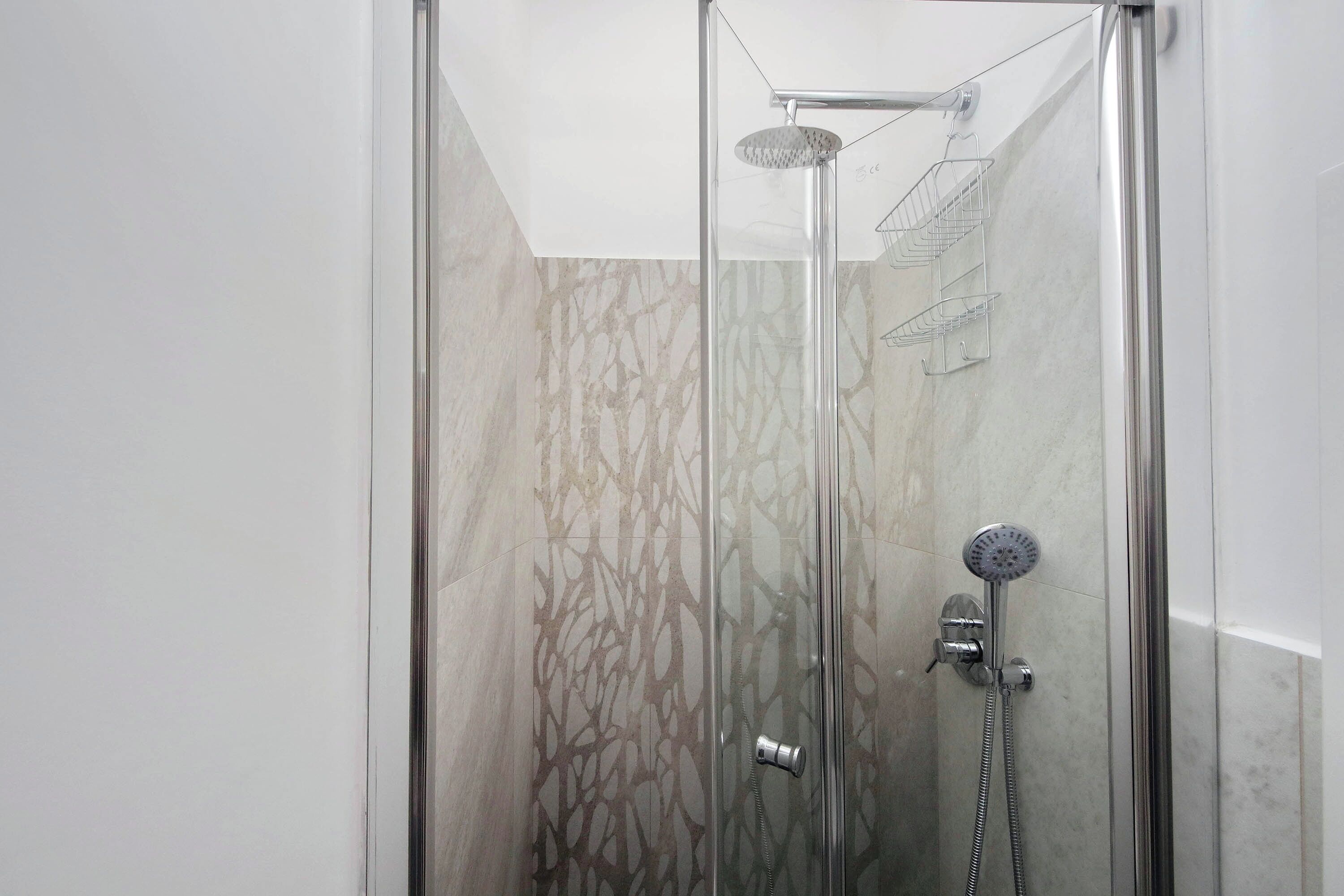 A glass-enclosed shower with a handheld showerhead and a wall-mounted faucet.