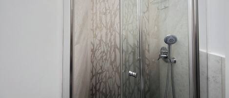 Une douche fermée par des parois en verre, dotée d’un pommeau de douche à main et d’un robinet mural.