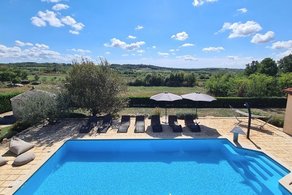 Ein Schwimmbecken mit Liegestühlen und Sonnenschirmen, umgeben von einem angelegten Garten und Blick auf die Landschaft.