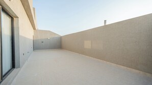 Un balcón moderno y limpio con suelo de baldosas, puerta de cristal y pared de hormigón.