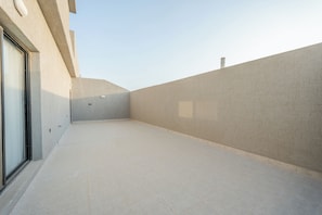 Ein gepflegter, moderner Balkon mit gefliestem Boden, einer Glastür und einer Betonwand.